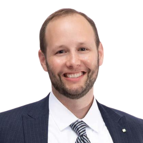 A man in a dark suit and striped tie smiles at the camera. He has short brown hair, a trimmed beard, and is posed against a white background.