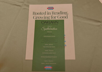 A green event program rests on a beige surface atop a flyer that reads Rooted in Reading, Growing for Good. The program lists activities and awards for a Spellabration event in Hot Springs, Arkansas.