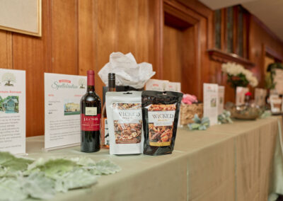 A display table with two bottles of wine, two bags of Wicked Mix snacks, informational pamphlets, and decorative items, set against a wooden-paneled wall.