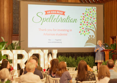 A woman speaks at a podium in front of a large screen displaying AR Kids Read Spellebration with a colorful tree graphic. Audience members are seated, and large white GROW letters are on the stage.